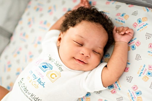 A smiling baby asleep in a safe crib.